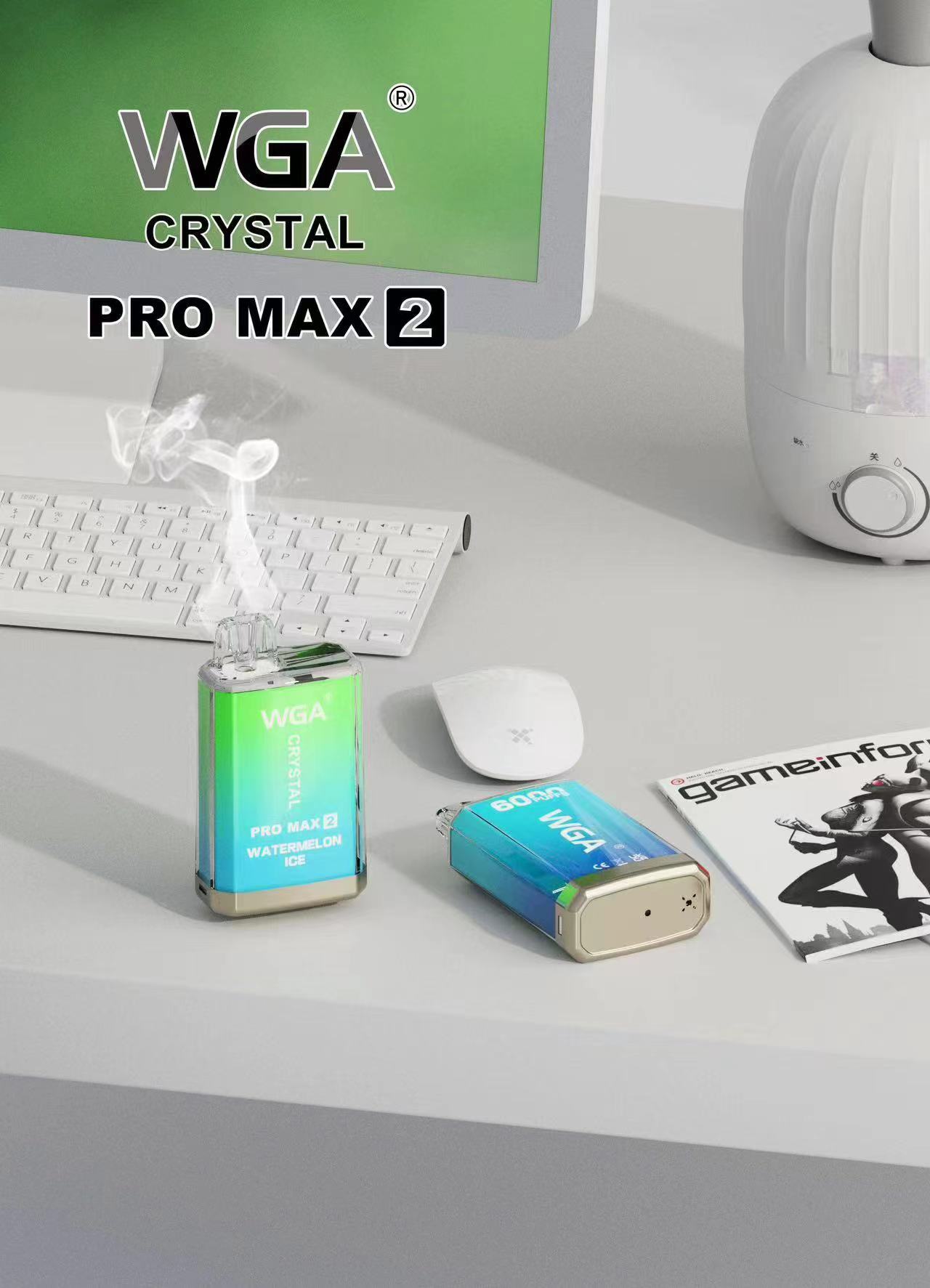 WGA Crystal Pro Max 2 vaping devices on a desk with a keyboard, mouse, and a magazine in the background. One device emits vapor.
