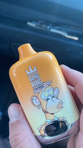 A hand holding a vibrant orange vape device featuring a cartoon monkey with sunglasses and a crown, with the text "BANG KING" and "Delphi Tech" printed on it.