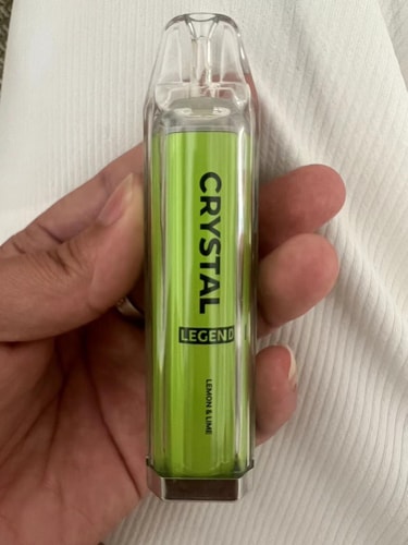 A hand holding a transparent disposable vape device labeled "Crystal Legend" in green, with "Lemon & Lime" flavor written at the bottom.