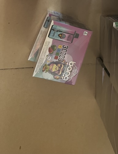 A box of "Bang" disposable vapes featuring colorful artwork and flavors including strawberry watermelon, kiwi passion fruit, and guava, displayed on a cardboard surface.
